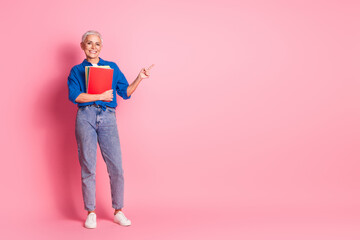 Full length photo of adorable good mood woman wear blue shirt holding book pile pointng empty space isolated pink color background
