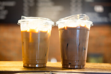 Two takeaway glasses filled with cold coffee with ice cubes on table