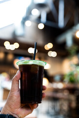 Hand holding a glass of iced black coffee at coffee shop.