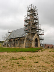 Kirche auf den Klippen von Étretat mit Baugerüst unter grauem Himmel
