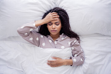 Young woman in polka dot pajamas relaxing in bed during morning in sunny bedroom