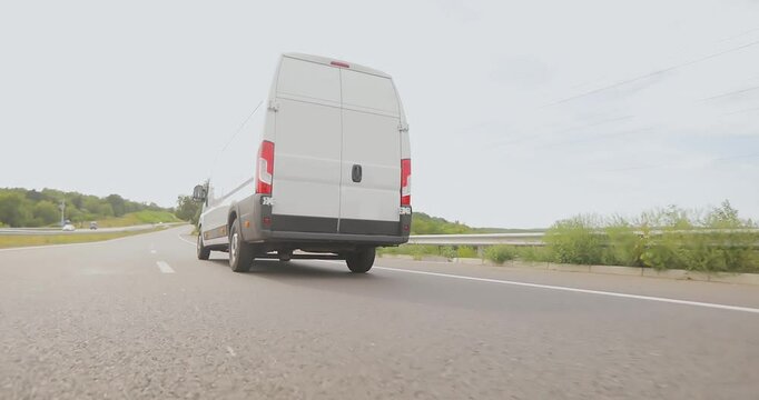 White service van drives on the highway in sunny weather. White delivery van driving along the highway. Cargo minibus drives on the highway.