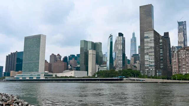 New York, USA, August 17, 2024. Beautiful footage along the bank of the East River, in front of us the Manhattan cityscape. On the left the skyscraper headquarters of the United Nations, zoomed in.