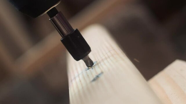Close-up of a screw being driven into a wooden plank by an electric screwdriver. The focus is on the screw and the tip of the screwdriver, capturing the precise moment of fastening