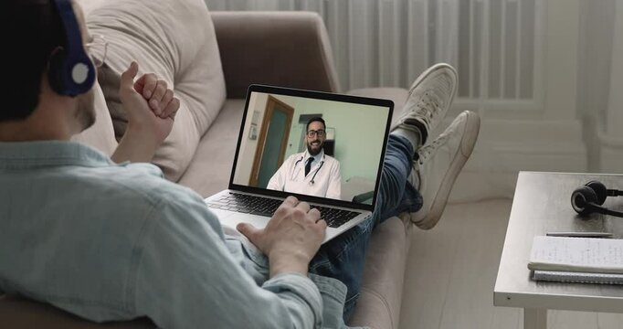 Man patient settled down on couch engaging in videocall on laptop, smiling young 35s doctor in white coat provide telemedicine consultation, virtual health checkup. Telemedicine and remote healthcare