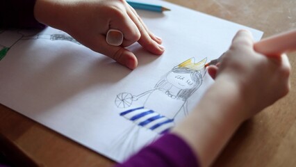 a child girl paints a princess crown on a sheet of paper with a felt-tip pen. close-up. kids leisure and hobbies © Natalia
