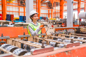 Smart Japanese female mechanical engineer is using a remote control to operate a crane or robot in a metal sheet factory. Female expert technical worker is using remote controller to control machine.