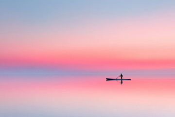 A man is paddling a kayak on a calm lake with a pink