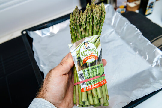Strasbourg, France - Sep 22, 2021: A bundle of fresh green asparagus labeled Asperges d'Alsace held above a foil-lined baking tray, showcasing local French produce.