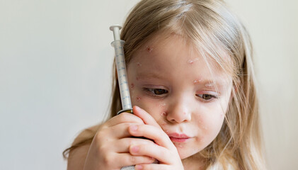 Viral disease. A sad little girl with a rash on her face from chickenpox holding medicine with a...