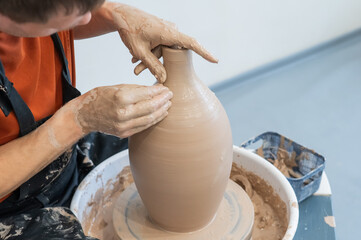 Close-up of a potter's hands making a ceramic vase on a potter's wheel. 