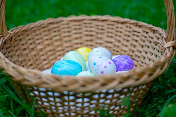 Wicker basket overflowing with colorful easter eggs in green grass