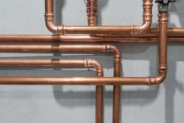Copper tubing of home heating system. Cooper pipes connected with pressed or crimped fittings create an industrial pattern on grey tiled wall background © GarkushaArt