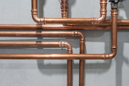 Copper tubing of home heating system. Cooper pipes connected with pressed or crimped fittings create an industrial pattern on grey tiled wall background