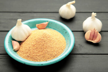 Garlic powder on plate on black wooden background, top view