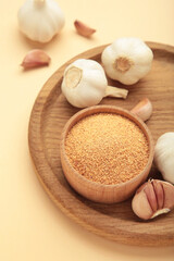 Fresh garlic and garlic powder in bowl on beige background. Using spices for meals. Top view