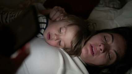 Mother and baby child lying in bed watching media entertainment at night