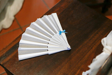 On a wooden table, there is a white fan adorned with a blue bow