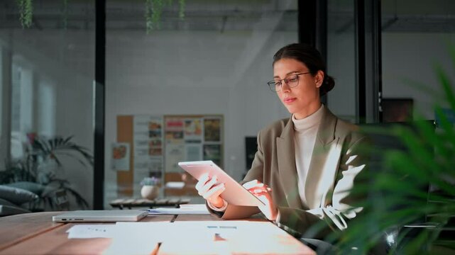 Young latin Hispanic young professional business woman working on touchscreen computer. Middle eastern businesswoman holding digital tablet using tab application sitting at desk workplace in office
