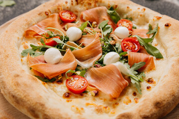 Gourmet pizza topped with fresh prosciutto, arugula, mozzarella, and cherry tomatoes on board