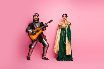 Lively Knight Playing Guitar for Princess in Costume Against Pink Backdrop