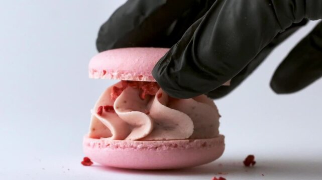 Close up footage of pastry chef hand in the black gloves joining pink macaroon cups together with its cream filling. Making macaroon dessert process on the white background