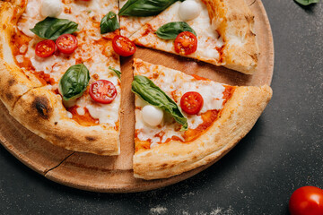 Freshly sliced Margherita pizza with basil, mozzarella, and cherry tomatoes on a rustic plate