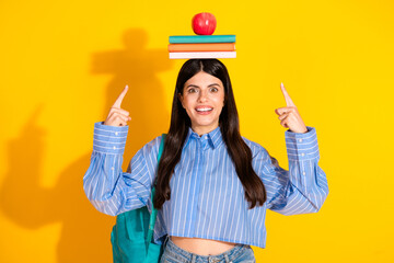 Young student balancing books and apple on head against vibrant yellow background