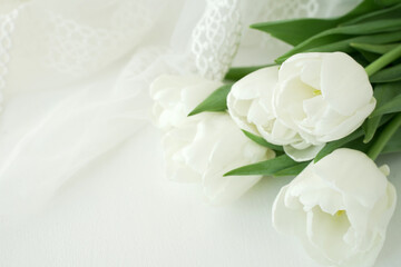 Lying bouquet of white tulips on the right of the picture, white elegant fabric background with lace, free space on the left, horizontal.   