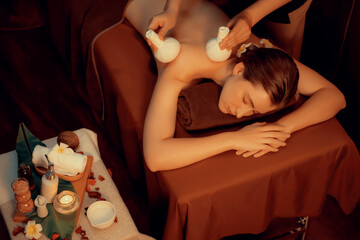 Hot herbal ball spa massage body treatment, masseur gently compresses herb bag on woman body....