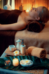 Aromatherapy massage ambiance or spa salon composition setup with focus decor candles and spa accessories on blurred woman enjoying blissful aroma spa massage in resort or hotel background. Quiescent