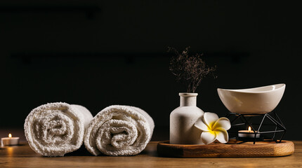 Obraz premium A set of cosmetics, burning candles, and a towel for spa treatments on a dark background, creating a serene atmosphere for relaxation and wellness.