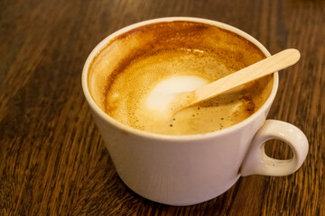 Cappuccino hot drink served in a china mug with wooden stirrer