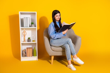 Young woman reading a book in a cozy chair against a vibrant yellow background