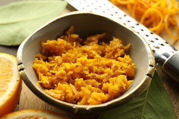 Orange zest, grater and fresh fruit pieces on table, closeup