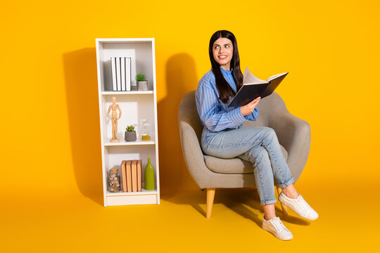 Young woman reading a book on a stylish chair with a yellow background and modern decor accents