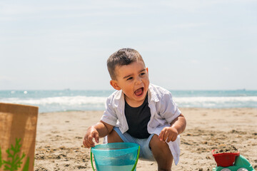 Toddler enjoying summer vacation, playing with beach toys on the sand near the sea