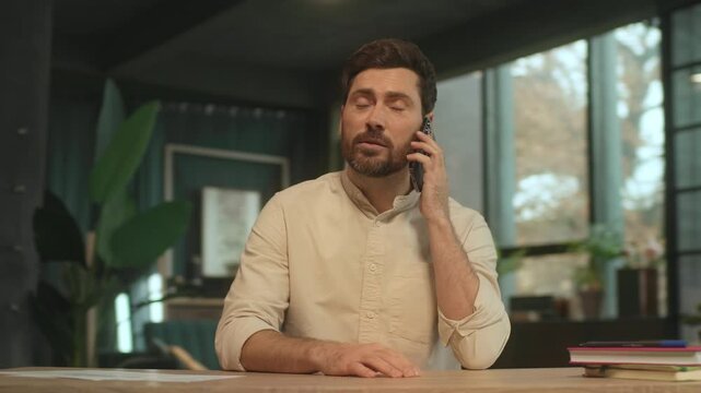 Handsome businessman sitting at desk talking on phone have conversation on smartphone smiling. Modern office. Social media.Camera moving around. 360 Degree