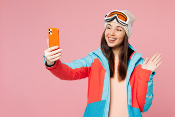 Skier young woman wear warm blue padded jacket ski goggles mask spend extreme weekend winter season in mountains do selfie shot on mobile cell phone isolated on plain pink background. Hobby concept. © ViDi Studio