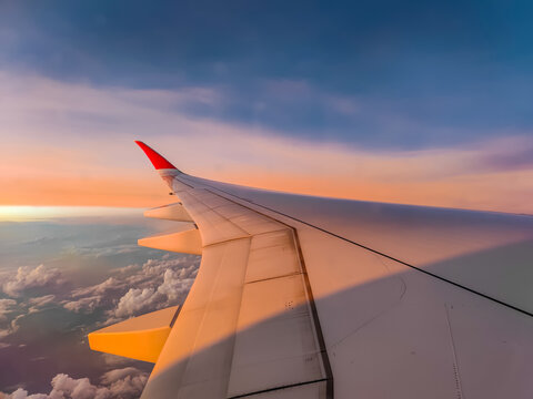The view from the airplane window to the clouds and sunset during a flight. Airplane wing above thick colourful clouds.  - Powered by Adobe