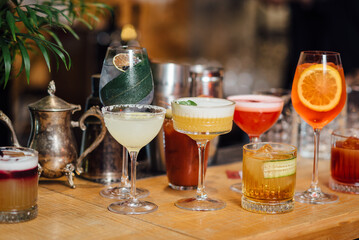 Сolorful cocktails close-up in elegant glassware, garnished with fruits and herbs, captured with a shallow depth of field for bokeh effect. Bright indoor bar setting with blurred background