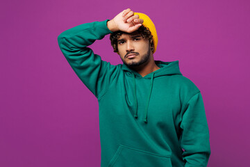 Young sad exhausted sick ill tired Indian man he wearing green hoody yellow hat casual clothes put...