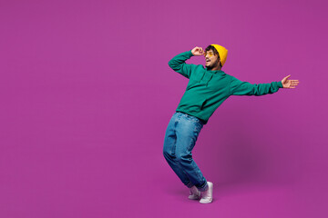 Full body side view young shocked fun Indian man in green hoody yellow hat sunglasses casual...
