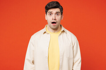 Young sad shocked scared astonished man he wearing white shirt yellow t-shirt casual clothes look camera with opened mouth isolated on plain red orange background studio portrait. Lifestyle concept.