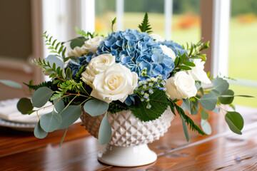 A sophisticated centerpiece featuring blue hydrangeas, white roses, and lush greenery, arranged in a textured white bowl, creating a timeless table display.
