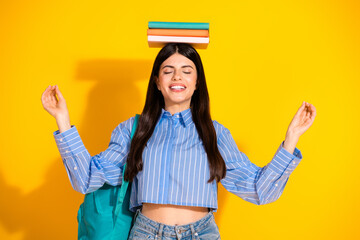 Young woman balancing books on her head against a vibrant yellow background
