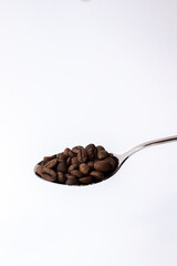 Freshly roasted coffee beans on a spoon, scattered elegantly on a clean white background.