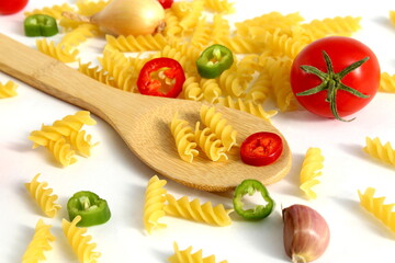 On a white background lies a wooden spoon with pasta and tomatoes.