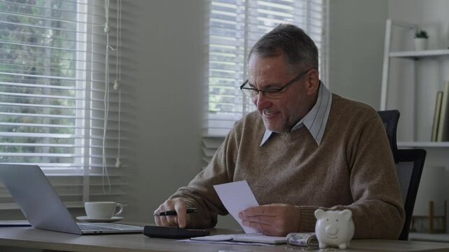 Old man using calculator to calculate personal finance, income, expenses for future plan. Concept of filing tax, tax deduction, tax payment and bill checking.