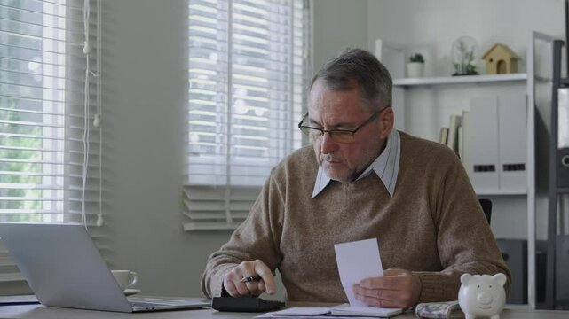 Old man using calculator to calculate personal finance, income, expenses for future plan. Concept of filing tax, tax deduction, tax payment and bill checking.